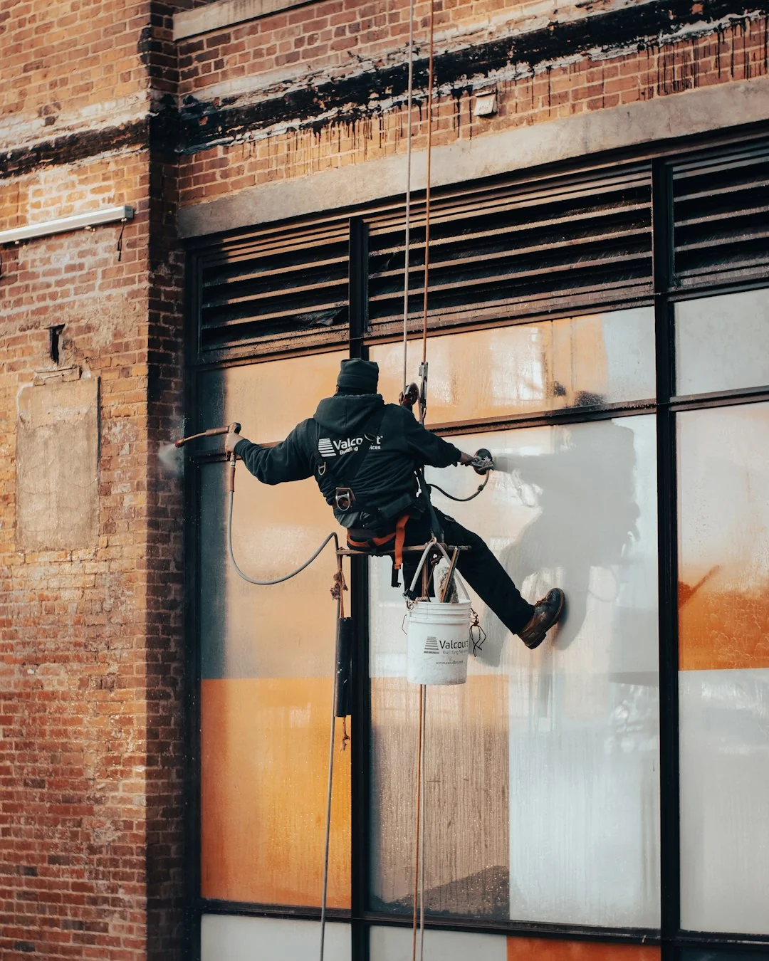 A male window cleaner washing the exterior glass roof from above with a tool during daylight.